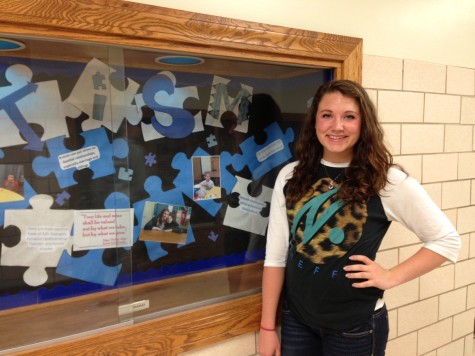 Junior Rachel Harris poses beside the display case outside of the high school main office.  Harris created the display, which is devoted to promoting autism awareness.