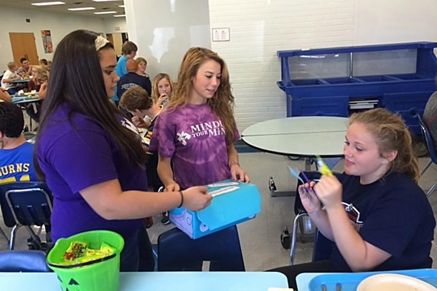 Freshmen Aedium members Paige Wenner and Tyson Irvin sell shoe cutouts to Kaitlyn Hoover at lunch to raise money for the Out of the Darkness Walk.