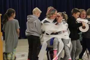 Second grade teacher Tara Naylor holds Maddie Shura as the two are toilet-papered as part of an award at the Myers Assembly to recognize International Childhood Cancer Awareness Week.